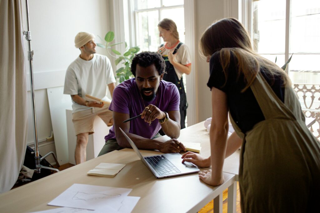 A Group Of Four People Collaborating Around A Table With A Laptop And Papers, Discussing The Legitimacy Of Digital Marketing In A Bright Room.